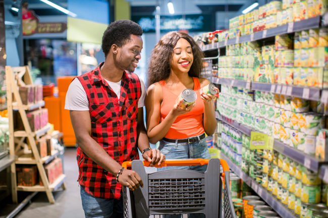 smiling young couple with shopping cart choosing food in supermarket